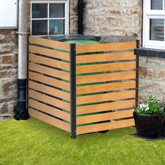 a wooden box sitting in the grass next to a brick building and potted plants