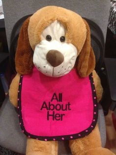 a stuffed dog wearing a pink bib that says all about her