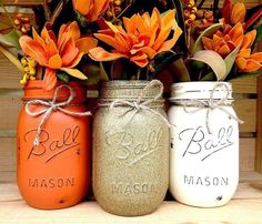 three mason jars with orange flowers in them sitting on a wooden table next to each other