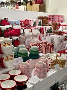 many cups and mugs are on display in a store with christmas themed items behind them