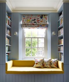 a window seat with bookshelves in front of it and a yellow cushion on the bottom