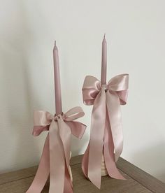 two pink candles with bows on them sitting on a table