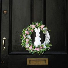 a wreath with a white bunny sitting on it's side next to a door