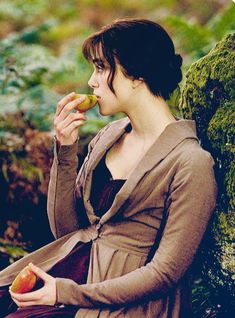 a woman sitting on a rock eating an apple