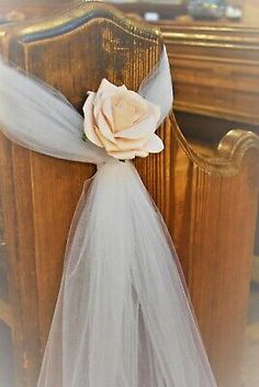 a white rose is attached to the back of a chair with tulle and ribbon