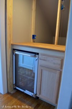 an empty refrigerator in the corner of a room with wood floors and cabinets around it