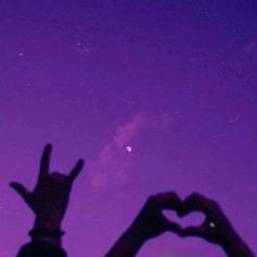 two hands making the shape of a heart in front of a purple and blue sky