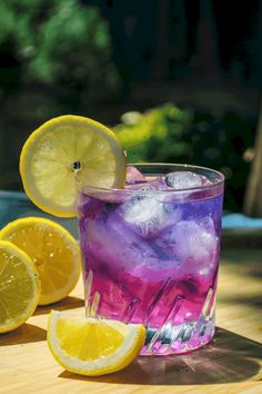 a glass filled with ice and lemons on top of a wooden table next to sliced lemons