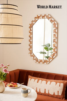 a mirror hanging on the wall above a table with food and flowers in front of it