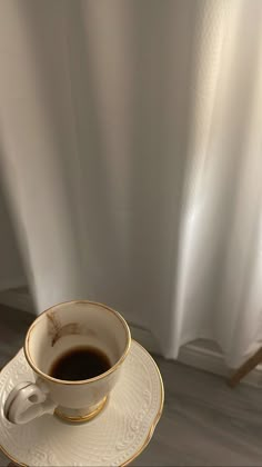 a cup of coffee sitting on top of a saucer next to a white curtain