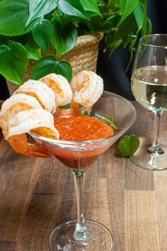 shrimp and sauce in a martini glass on a wooden table next to a potted plant