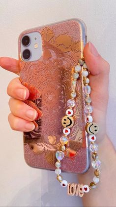 a woman holding up her phone case with beads and charms attached to the back of it