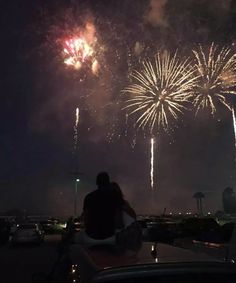 fireworks are lit up in the night sky above cars and people sitting on top of a car