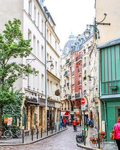 people are walking down the street in an old european city with tall buildings on either side