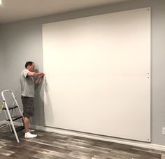 a man standing next to a whiteboard on top of a hard wood floor in an empty room