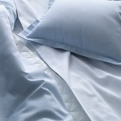 an unmade bed with blue sheets and pillows on it's side, close up