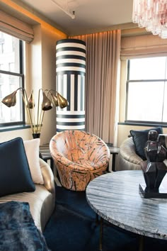 a living room filled with furniture next to two large windows and a round coffee table