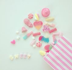 there are many different candies on the table next to a pink and white striped bag