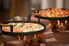 two pizzas sitting on top of wooden trays with candles in the back ground