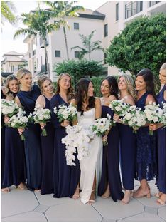 a group of women standing next to each other in front of a building holding bouquets