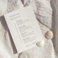 a wedding weekend program and seashells on a white sheeted bed with linen