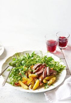 a white plate topped with meat and veggies next to two glasses of wine