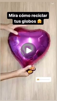 someone holding a purple heart shaped balloon in front of a wooden table with text that reads mira como reciclar tus globos