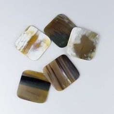 four square pieces of agate glass sitting on top of a white surface with brown and black stripes