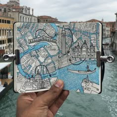 a hand holding up an open notebook with a map on it in front of the water