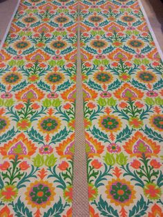 an orange and green floral pattern on the floor next to a white rug with pink flowers