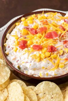 a bowl filled with corn and cheese surrounded by crackers on a plate next to chips