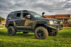 a black truck parked on top of a lush green field next to a brown house