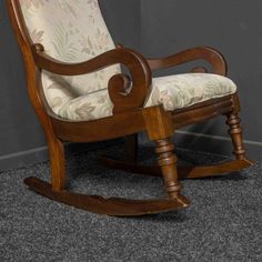 a wooden rocking chair sitting on top of a carpeted floor next to a wall