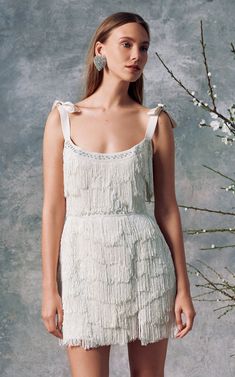 a woman standing in front of a plant wearing a white dress with fringes on it