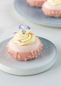 two plates with small desserts on them, one has a purple pansy and the other is white