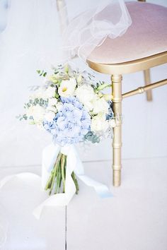 a bouquet of blue and white flowers sits on a chair with a veil draped over it