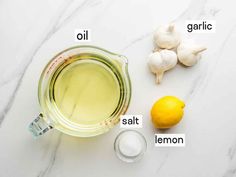 ingredients to make lemon garlic oil laid out on a white marble counter top with the names