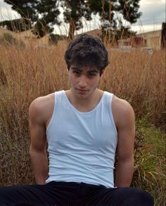 a young man sitting on the ground in front of tall grass