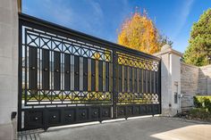 an iron gate is shown in front of a white building with autumn leaves on the trees