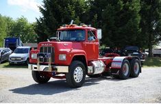 a red mack truck parked in a parking lot next to other trucks and trees on a sunny day