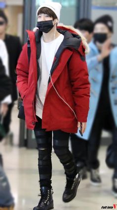 a man in a red coat and black pants wearing a face mask while walking through an airport