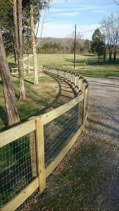 a wooden fence next to a road in the middle of a field with trees on both sides