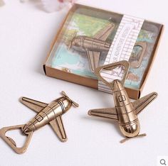 two gold colored metal airplane shaped paper clips in front of a box with money inside