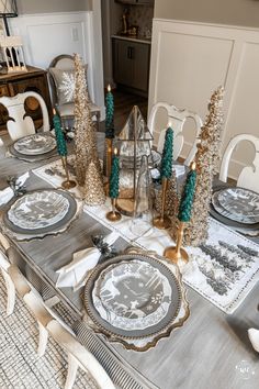 a dining room table set for christmas with silver and white plates, candles and napkins