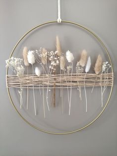 a circular metal rack with dried flowers on it hanging from the wall in front of a gray wall