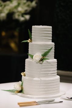 a wedding cake with white flowers and greenery on top is ready to be cut