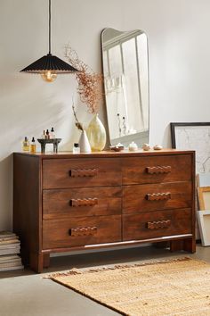 a wooden dresser sitting in front of a mirror and vase on top of it next to a rug