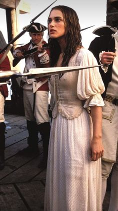 a woman in a white dress standing next to two men with swords on their shoulders