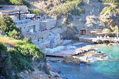 an outdoor area with chairs and tables next to the water in front of a rocky cliff