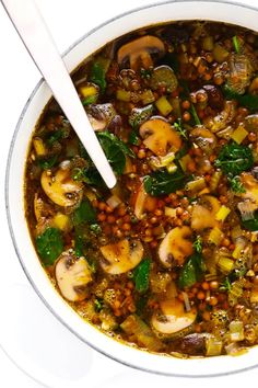 a white bowl filled with vegetables and lentils on top of a table next to a spoon